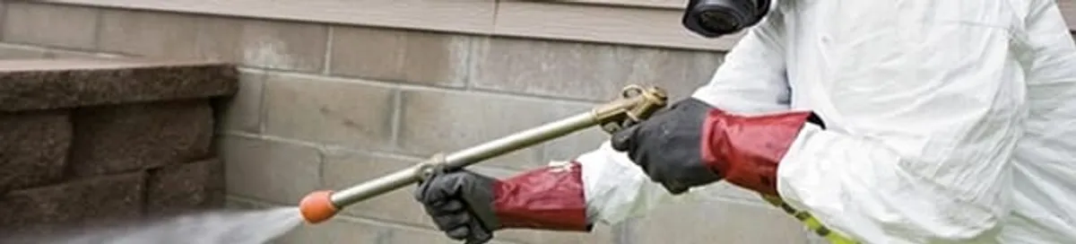 Pest control technician applying exterior insect treatment along a home foundation in Dallas, TX