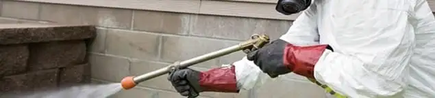 Pest control technician applying exterior insect treatment along a home foundation in Dallas, TX