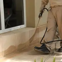 General pest control technician spraying exterior perimeter around a home in Dallas, TX