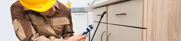 Roach exterminator applying treatment under kitchen cabinets in Dallas, TX