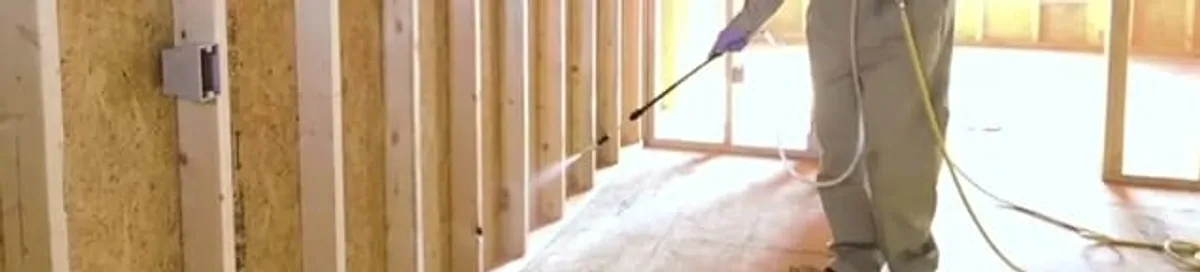 Termite treatment technician applying spray along framing and unfinished walls in Dallas, TX