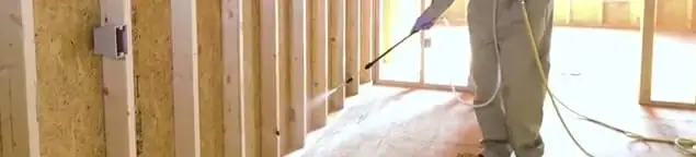 Termite treatment technician applying spray along framing and unfinished walls in Dallas, TX